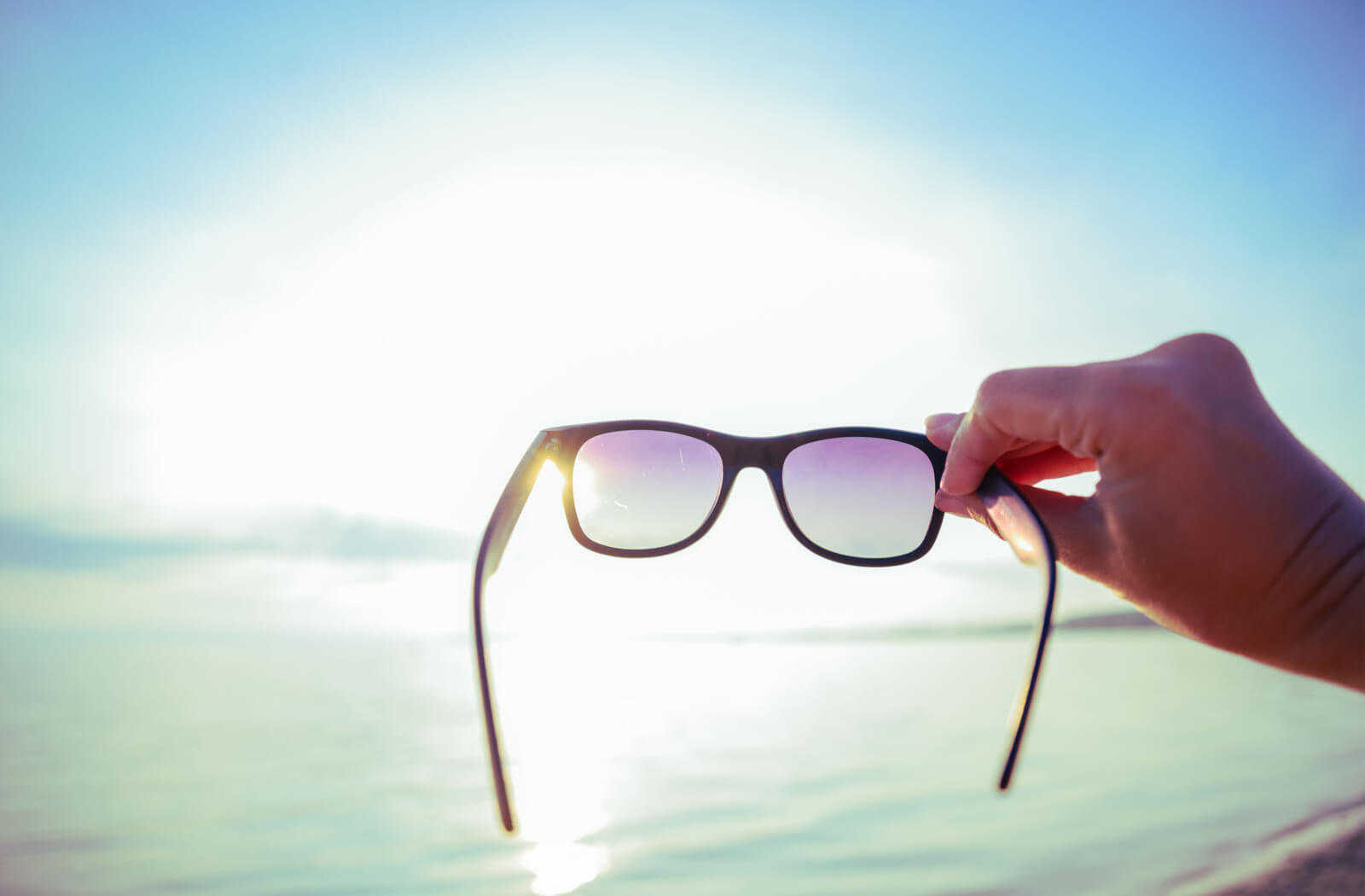 Close-up of a man's hands holding a polarized sunglasses directly into the sun.