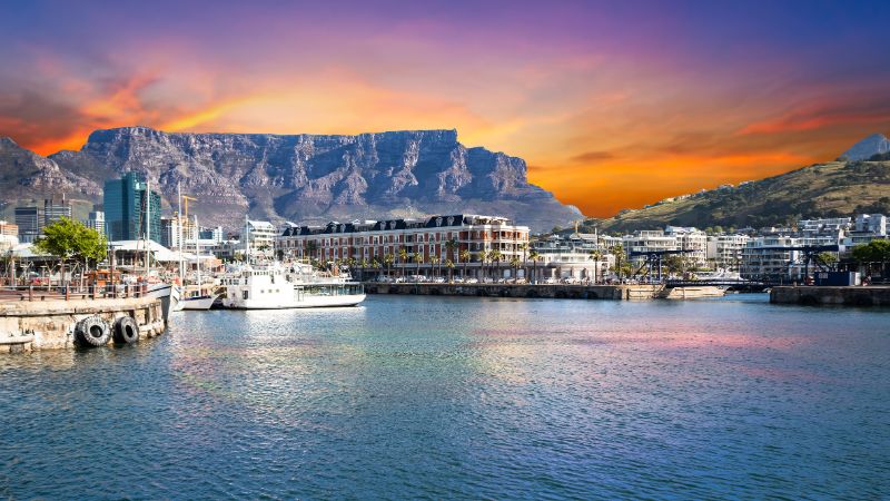 Victoria & Alfred Waterfront in Cape Town, set against a stunning backdrop of Table Mountain under a fiery sunset.