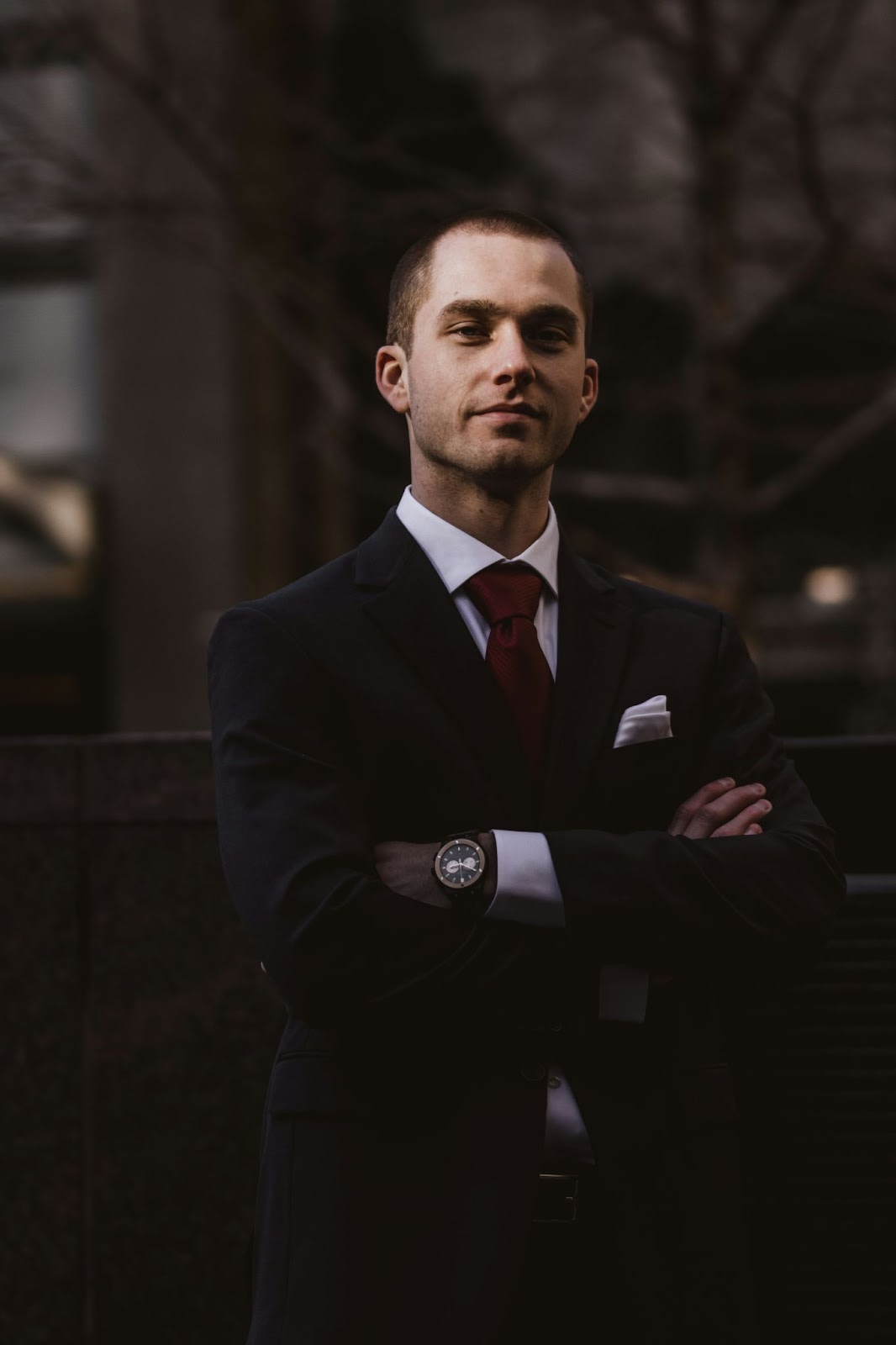 A man in a classic combination of neutral colours standing with crossed arms to convey confidence and strength through his professional headshots.