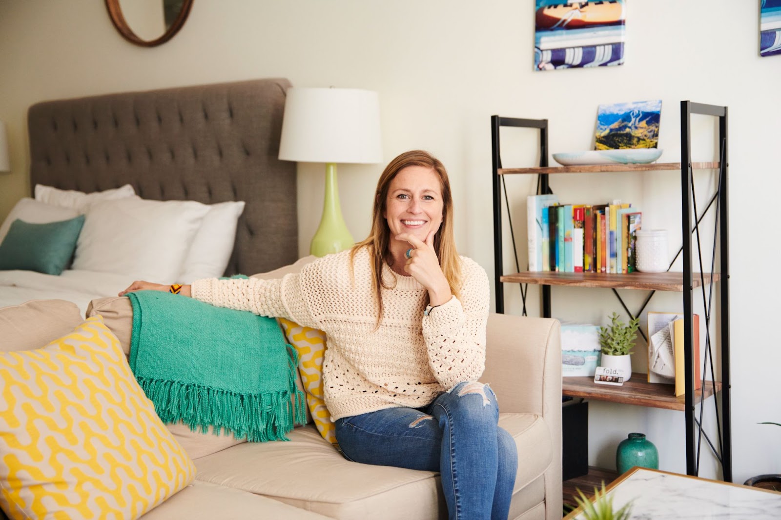 Woman in a tan shirt sitting on her couch smiling. 