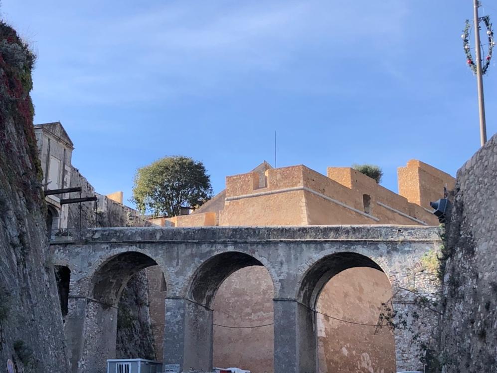 A stone archways with a building in the background

Description automatically generated