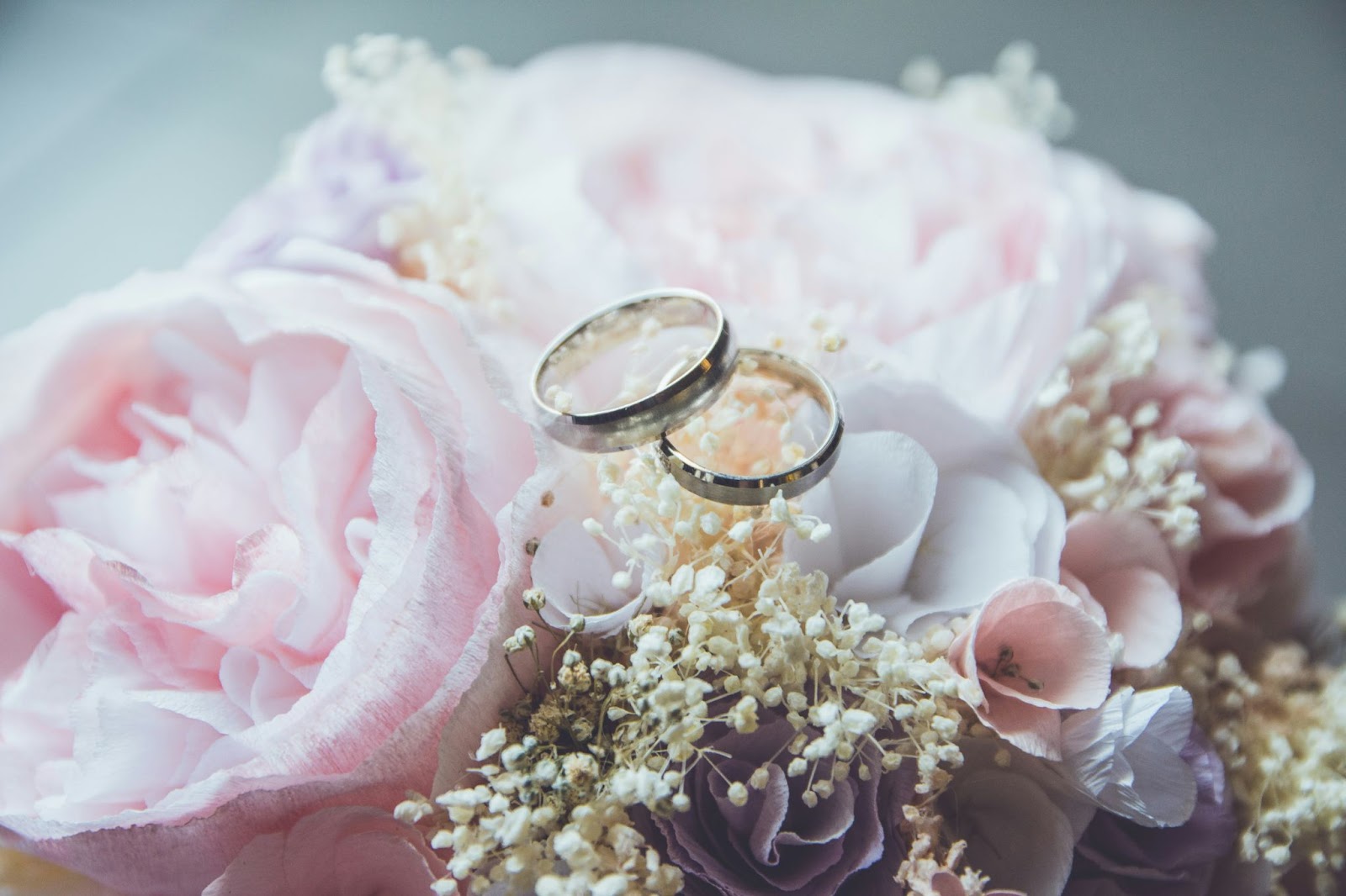 Two silver matching wedding bands laying on a bouquet of pink flowers.