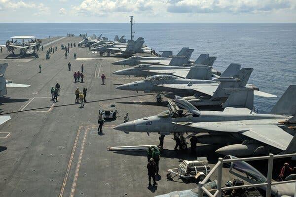 Rows of fighter jets are seen on the tarmac of an aircraft carrier in the middle of the ocean.