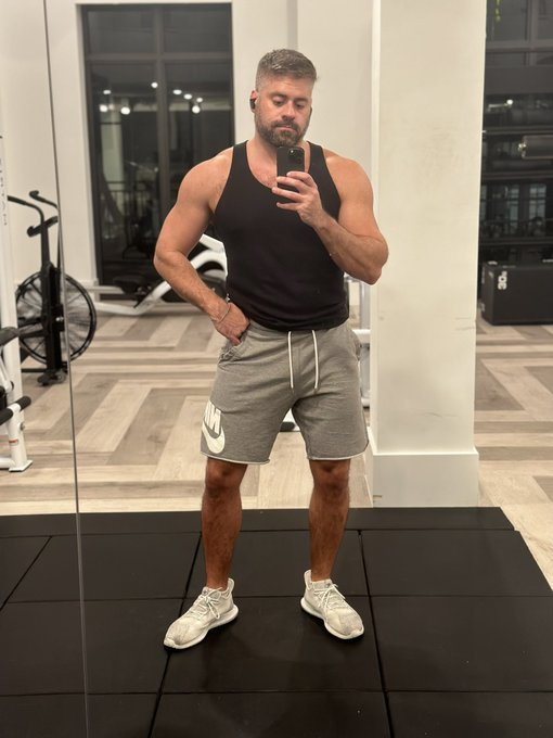 Max Romano taking a mirror iphone selfie at the gym in grey sweat shorts and black tank top