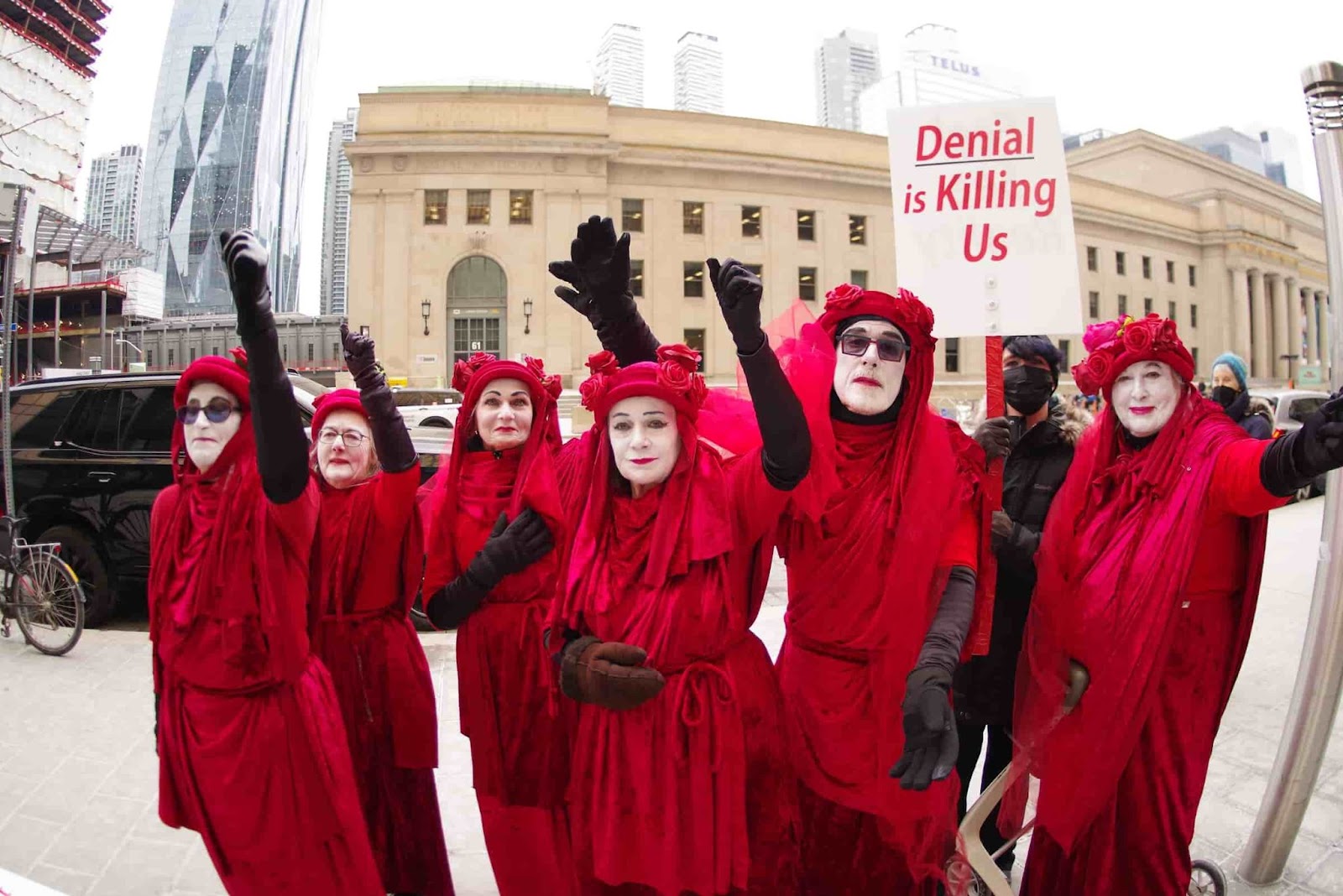 Red rebels point to the bankers while holding a sign saying denial is killing us