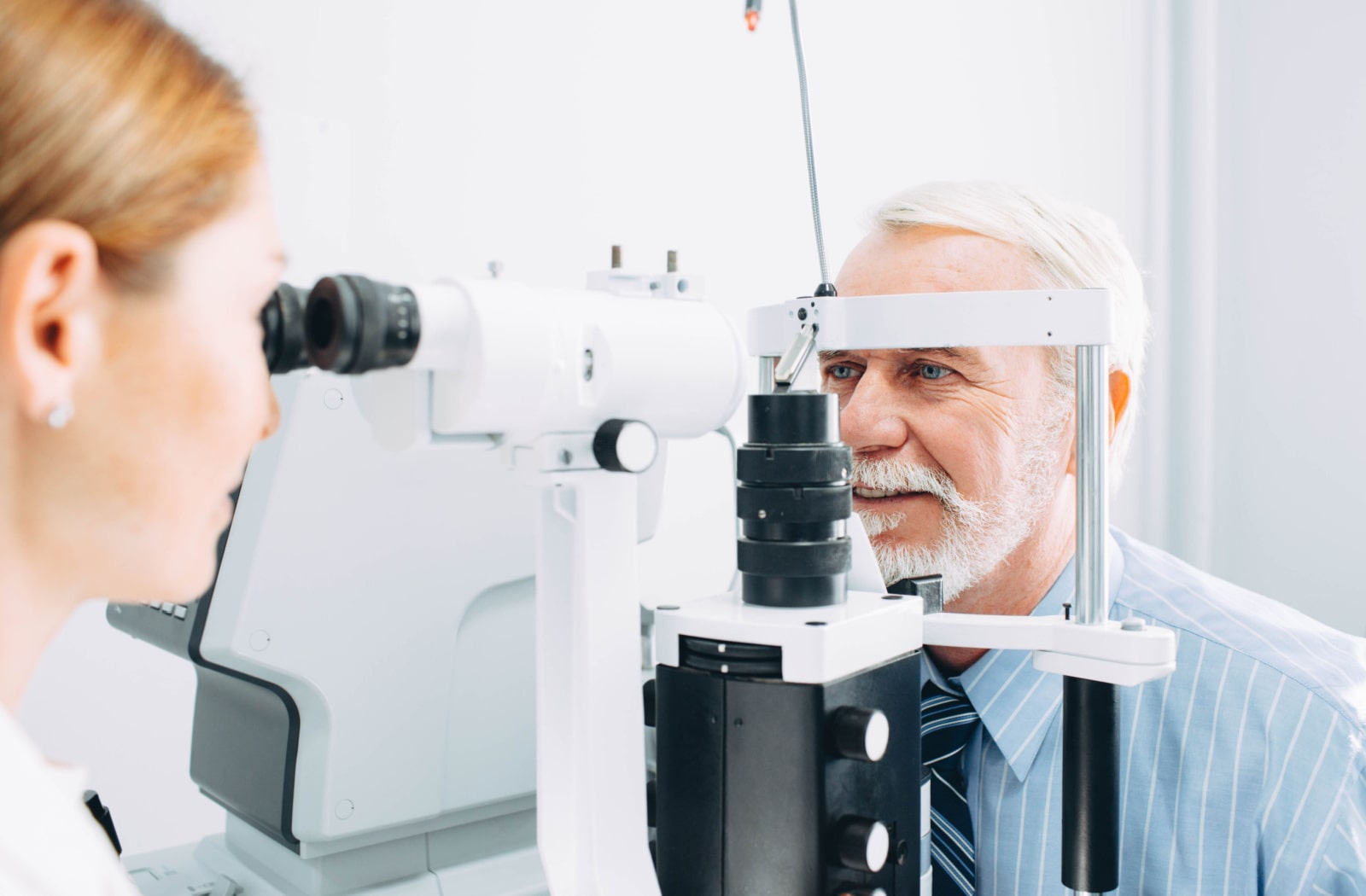 A female optometrist examining a male patient's eyes with a slit lamp