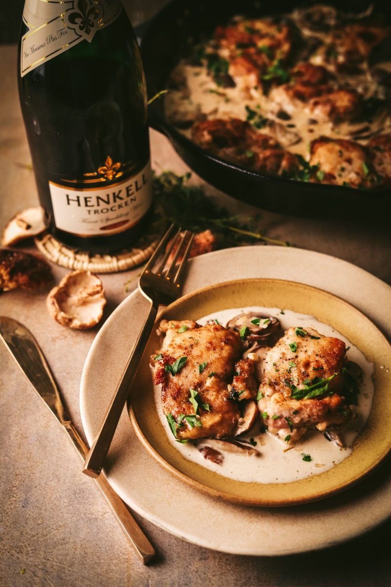 A plate of chicken with mushrooms and a bottle of champagne.
