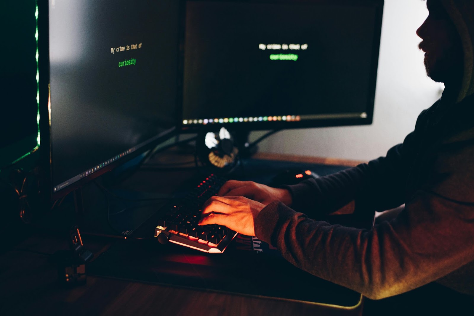 A person typing on a backlit keyboard in a dark room with a computer screen displaying the text