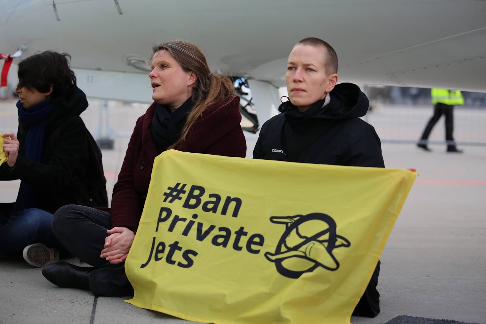 3 female scientists sit on a runway beside a private jet 