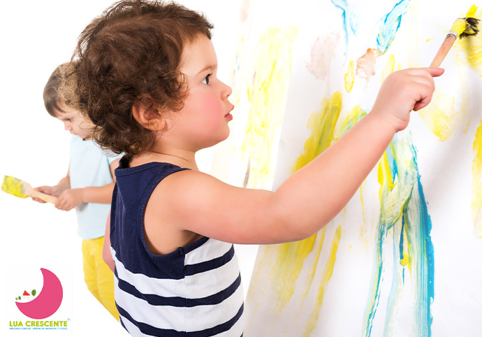 duas crianças a fazerem uma pintura com várias cores
