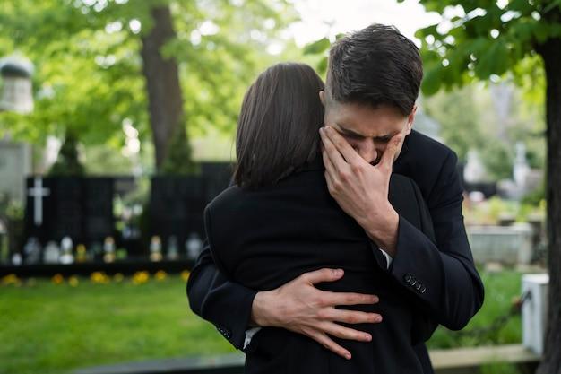 Free photo crying man and woman embraced at the cemetery