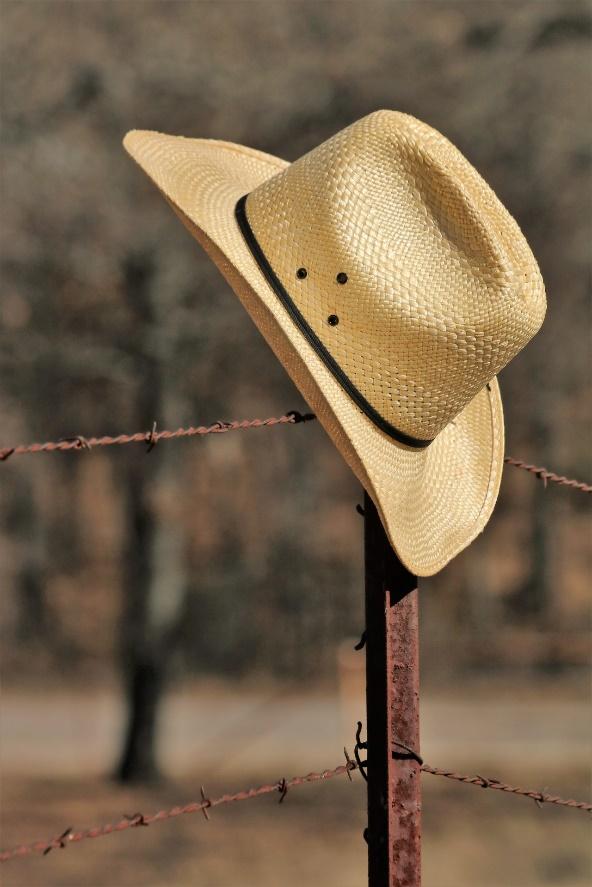 Close-up de um chapéu de cowboy de palha amarela pendurado em uma cerca de arame farpado enferrujado no país.