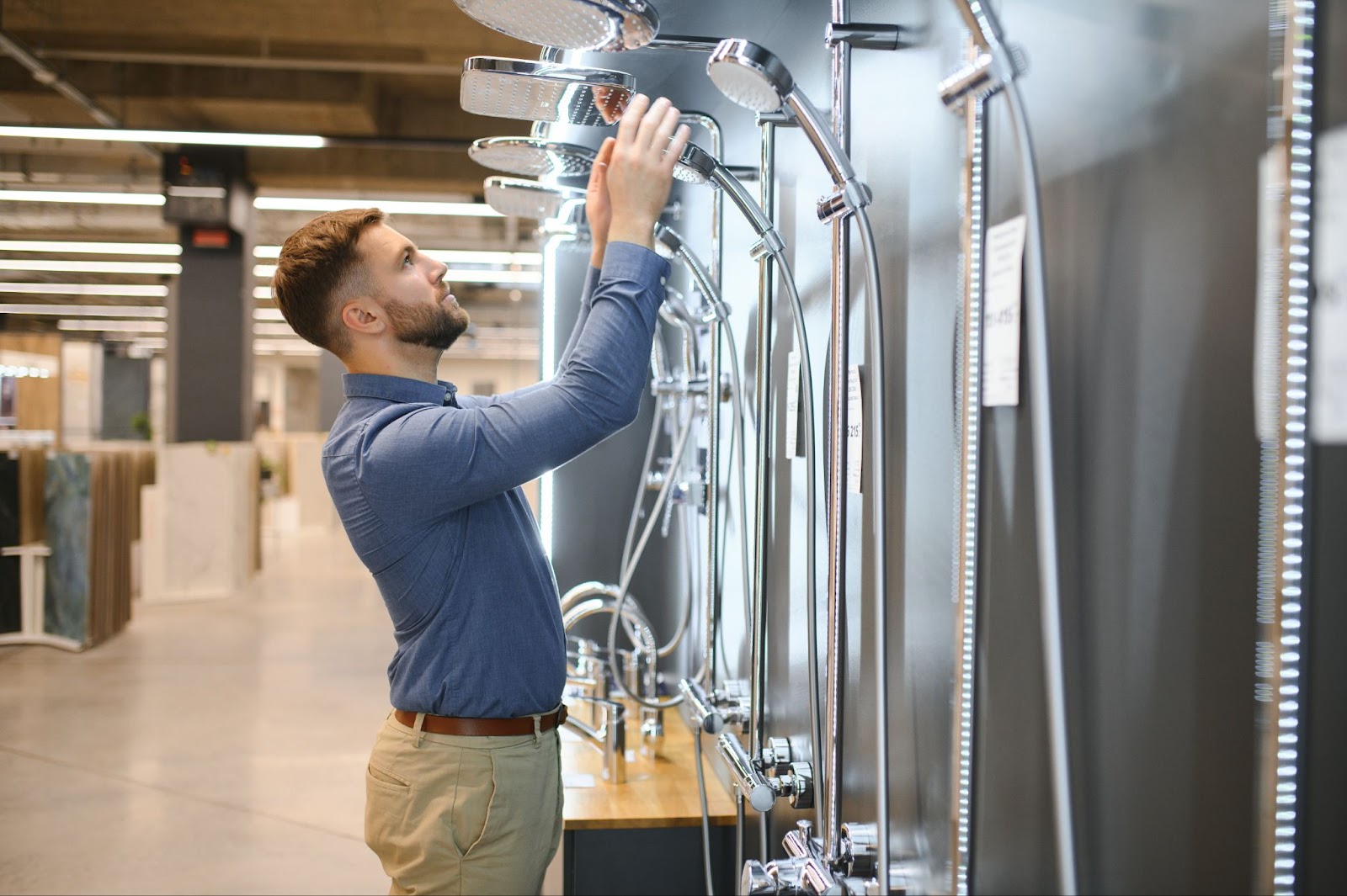 A male customer is choosing the right shower faucet from an array of options in a bathroom fixtures store.
