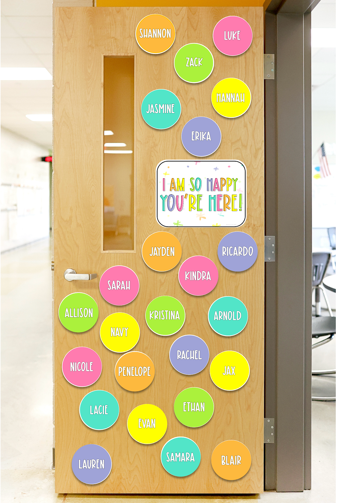 This image shows a classroom door decorated with bright, colorful circles. Each circle reads a student's name. In the middle of the door is a poster that reads "I am so happy you're here!" 