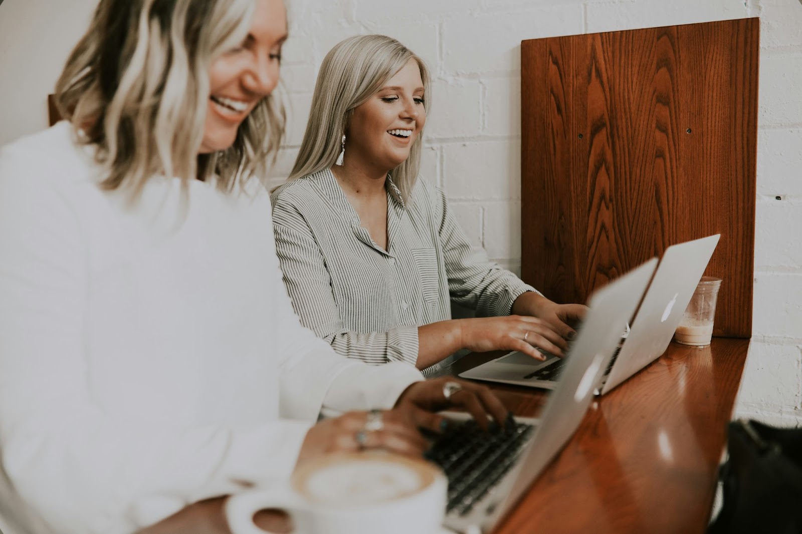 Two laughing women working on laptops developing their careers in HR