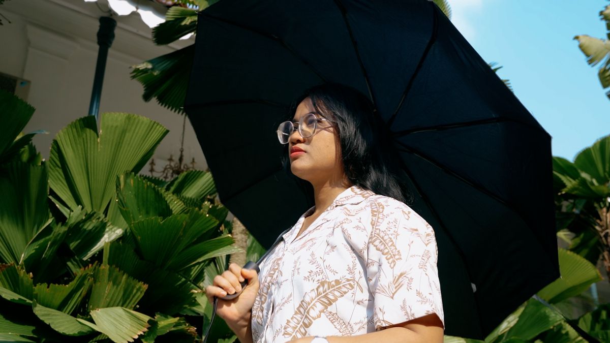 Mengapa cuaca Jakarta terasa panas? Foto seorang perempuan sedang memakai payung di bawah terik matahari, sekitarnya ada tumbuhan hijau