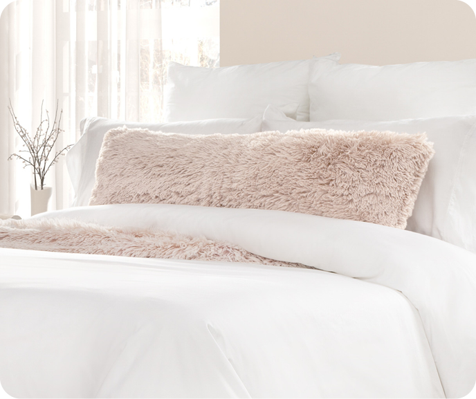 Our pink Frosted Lumbar Pillow in Woodrose shown on a bed with white bedding.