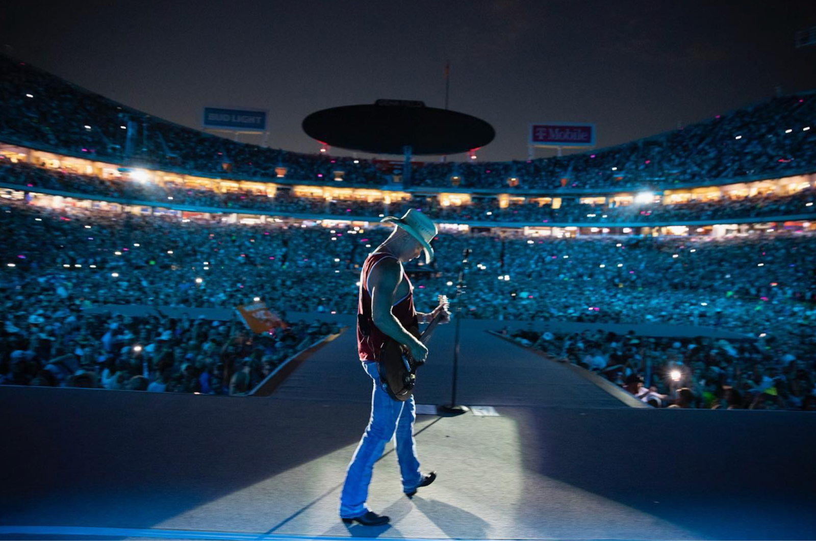A photo taken behind singer Kenny Chesney on stage performing in front of a live audience.