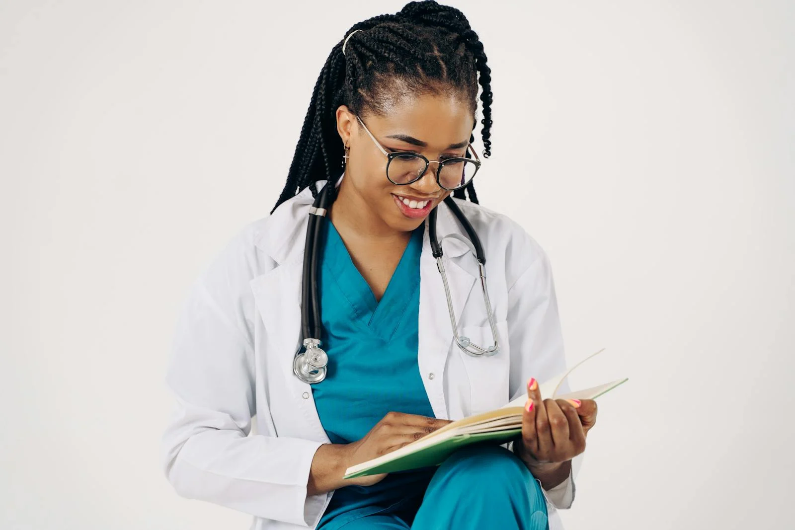 Black doctor in uniform with braids and glasses sitting and smiling at a book - 10 Healthcare Jobs You Should Know About 