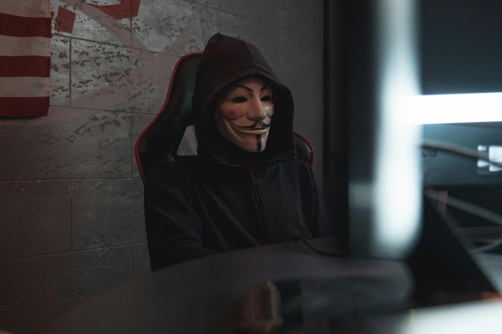 A man dressed in black with a hood and mask, sitting in front in a gaming chair