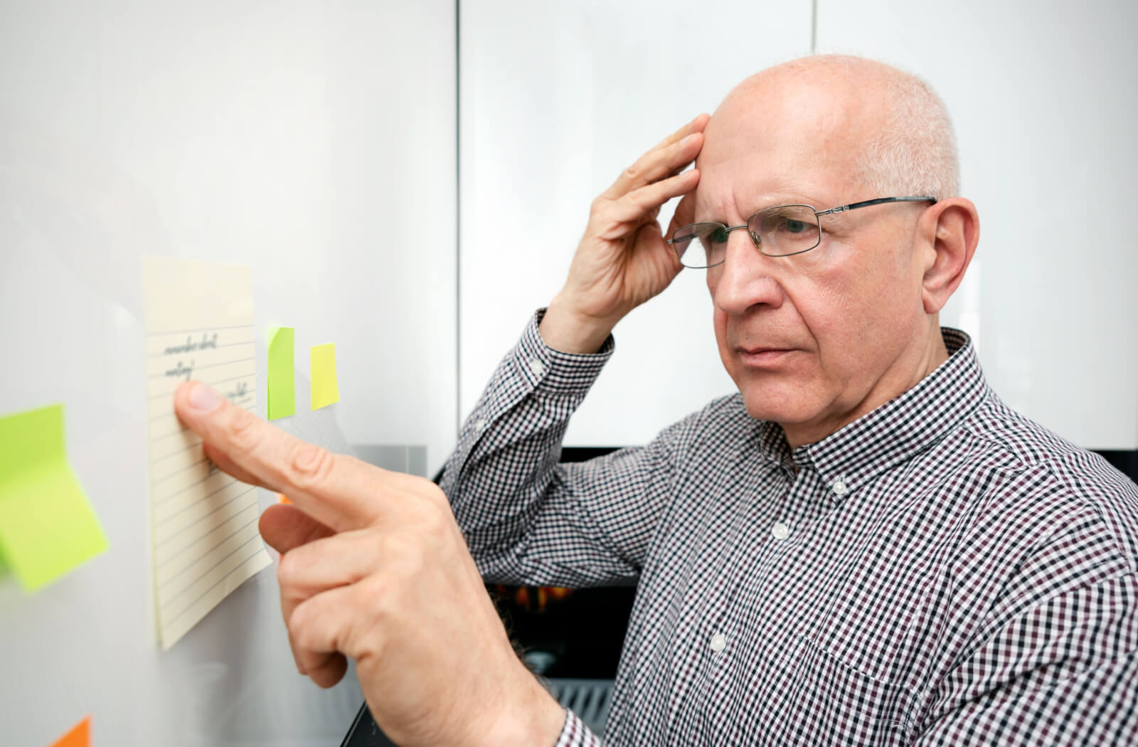 A senior man trying to remember what the reminder on the sticky note is for.