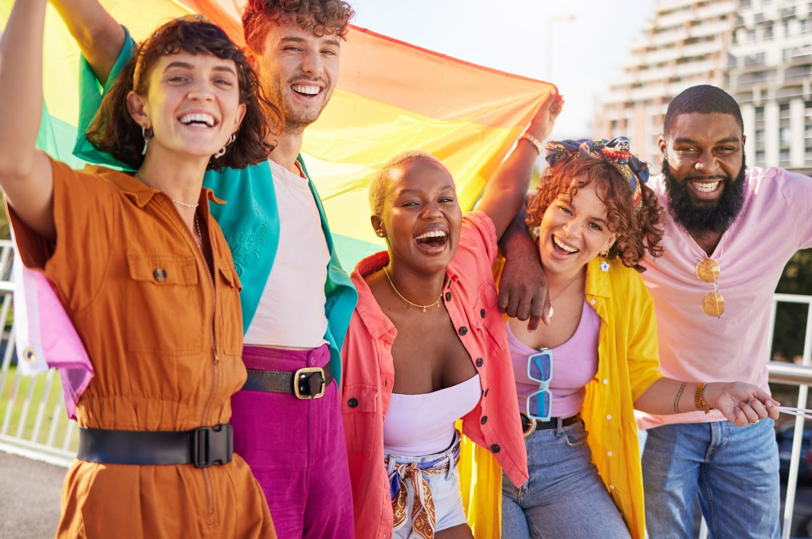 Grupo diverso de cinco pessoas sorrindo enquanto seguram uma bandeira LGBT+.