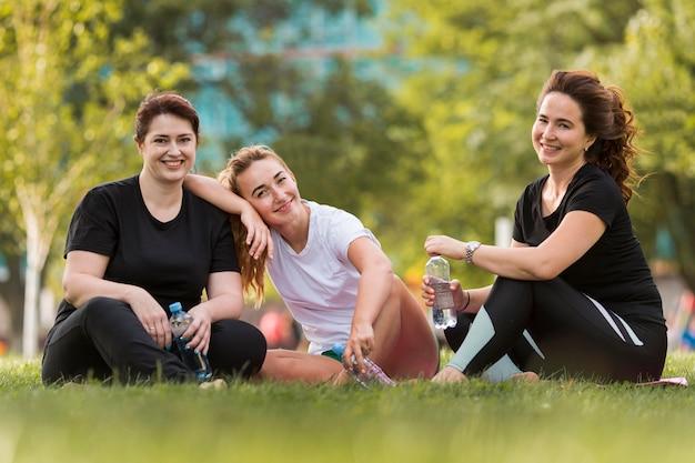 Free photo front view best friends sitting on grass while wearing sportswear