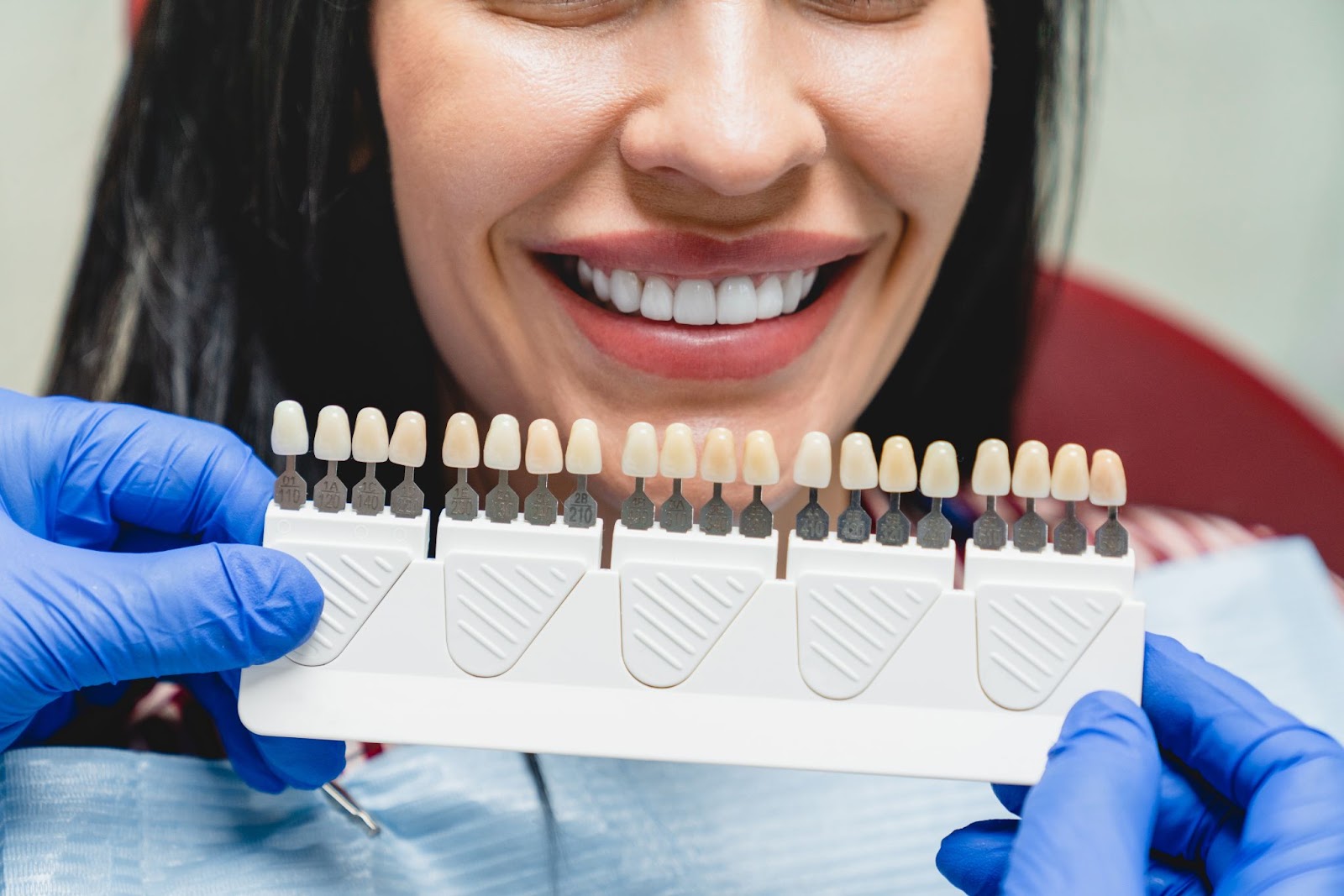 Smiling woman getting matched with the correct shade of teeth for dental crowns 