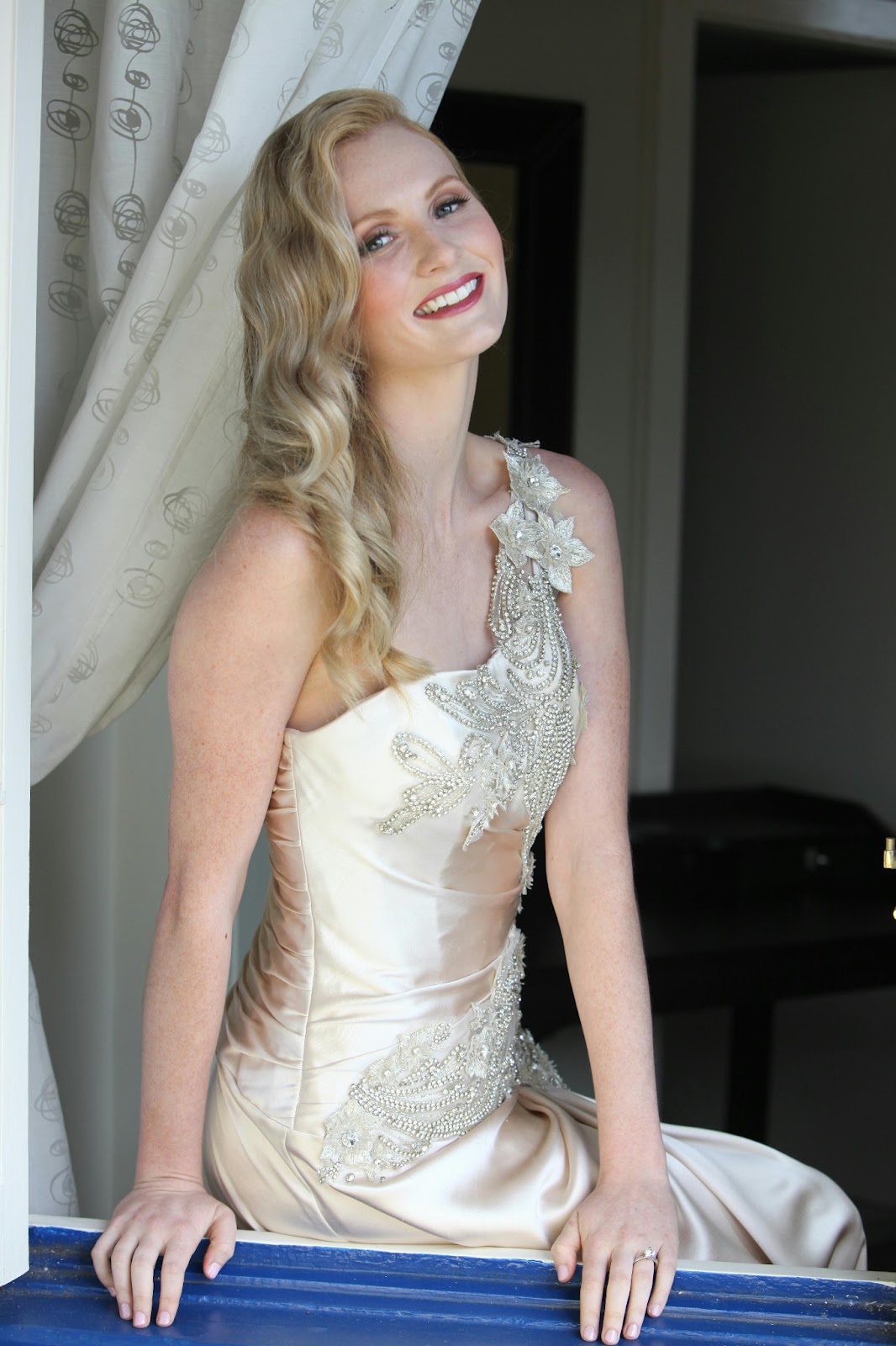 A bride sitting near a sandy beach, wearing a one-shoulder modern gown with a sparkling jeweled waistband.