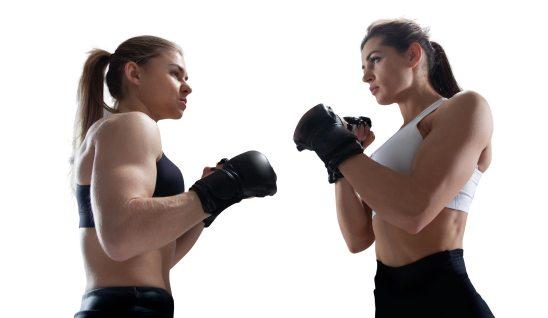 Two female MMA fighers holding fists up against white background