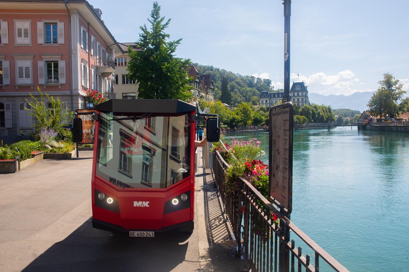 A red bus on the sidewalk next to a body of water

Description automatically generated