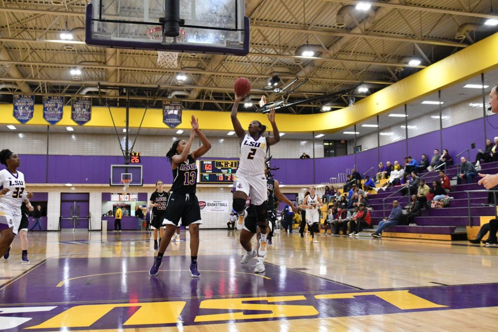 A photo of LSUS men's basketball team in action, featuring several players in blue and white uniforms playing basketball on a basketball court with spectators in the background.