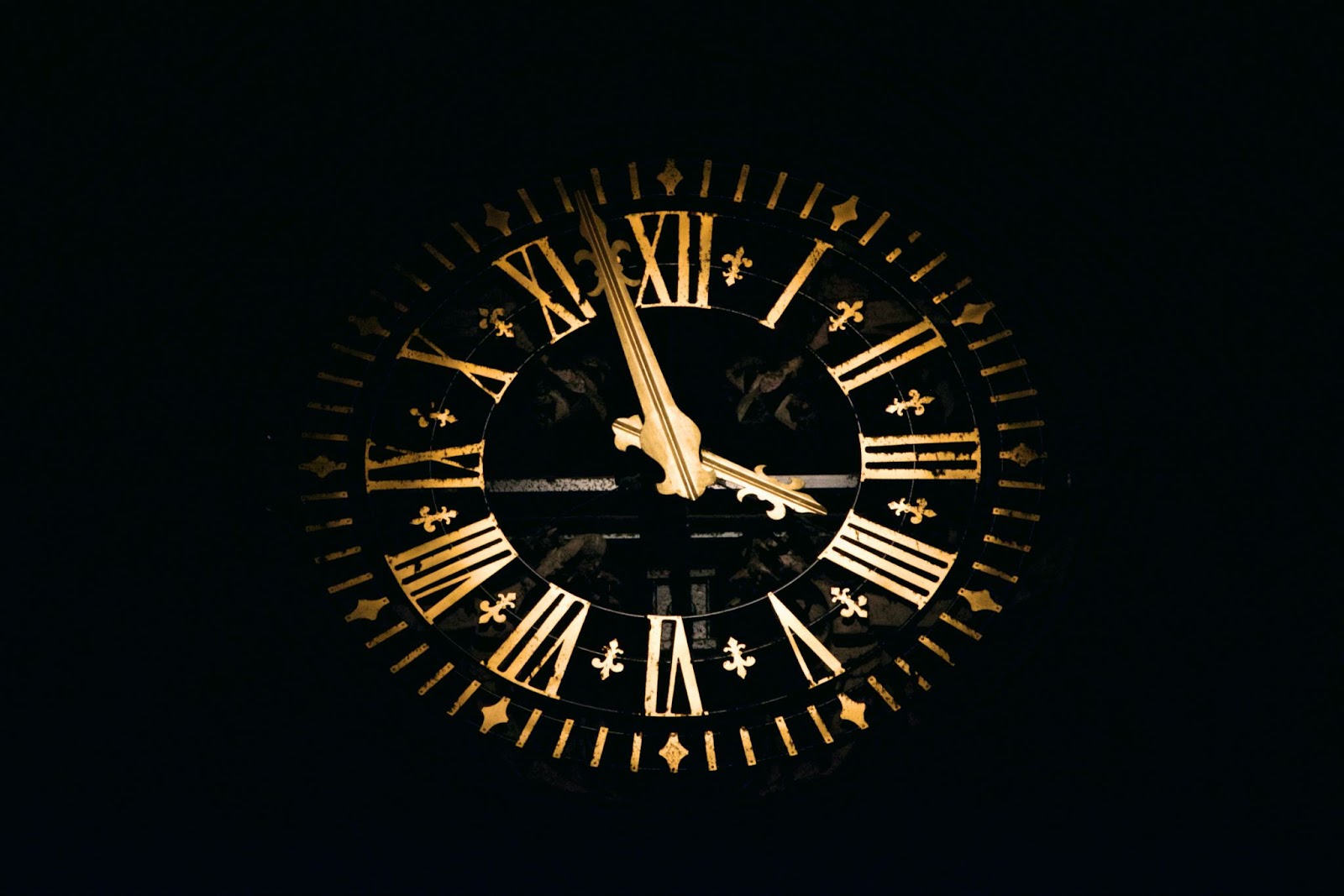 A glowing, golden clock showing the hours in roman numerals set against a black background.