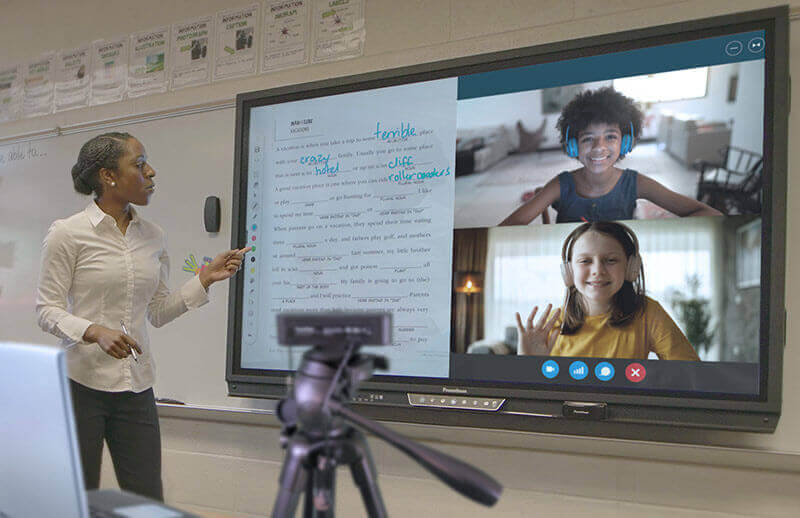 Une professeure donne un cours en distanciel à ses élèves grâce à un écran numérique interactif ActivPanel et une caméra de visioconférence.  