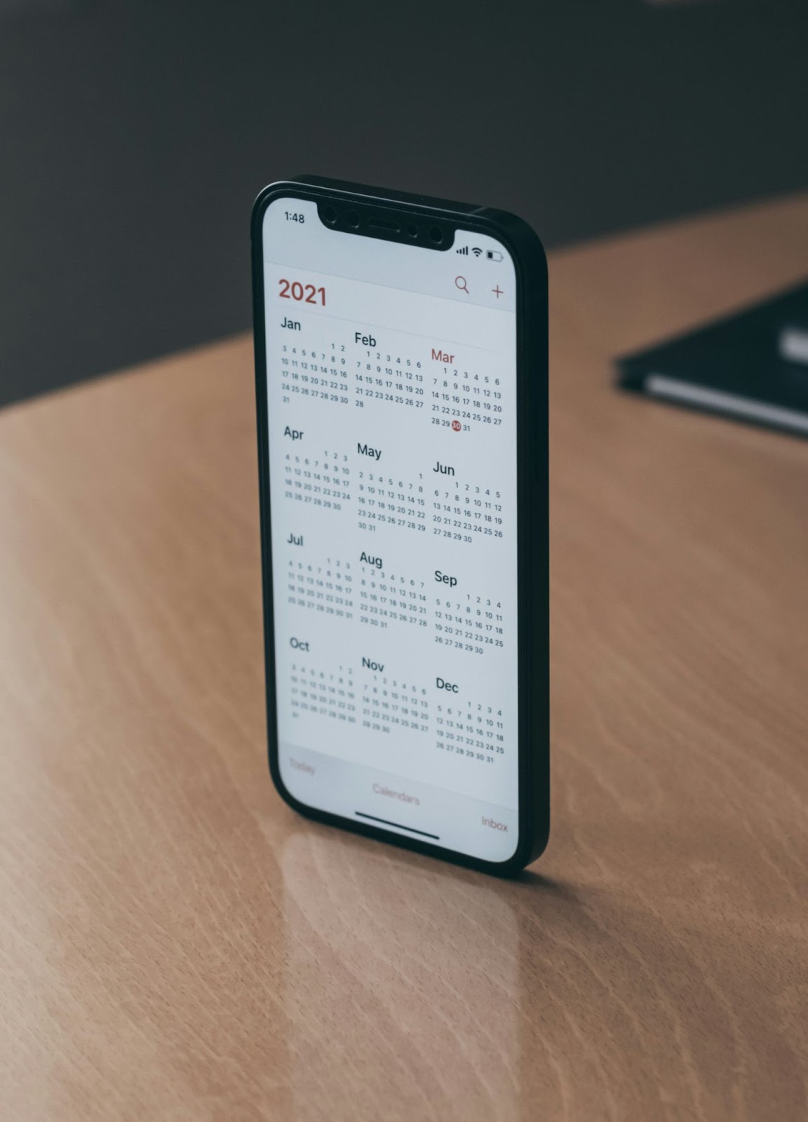 A phone balanced standing on a desk, showing the year 2021 month by month, day by day.