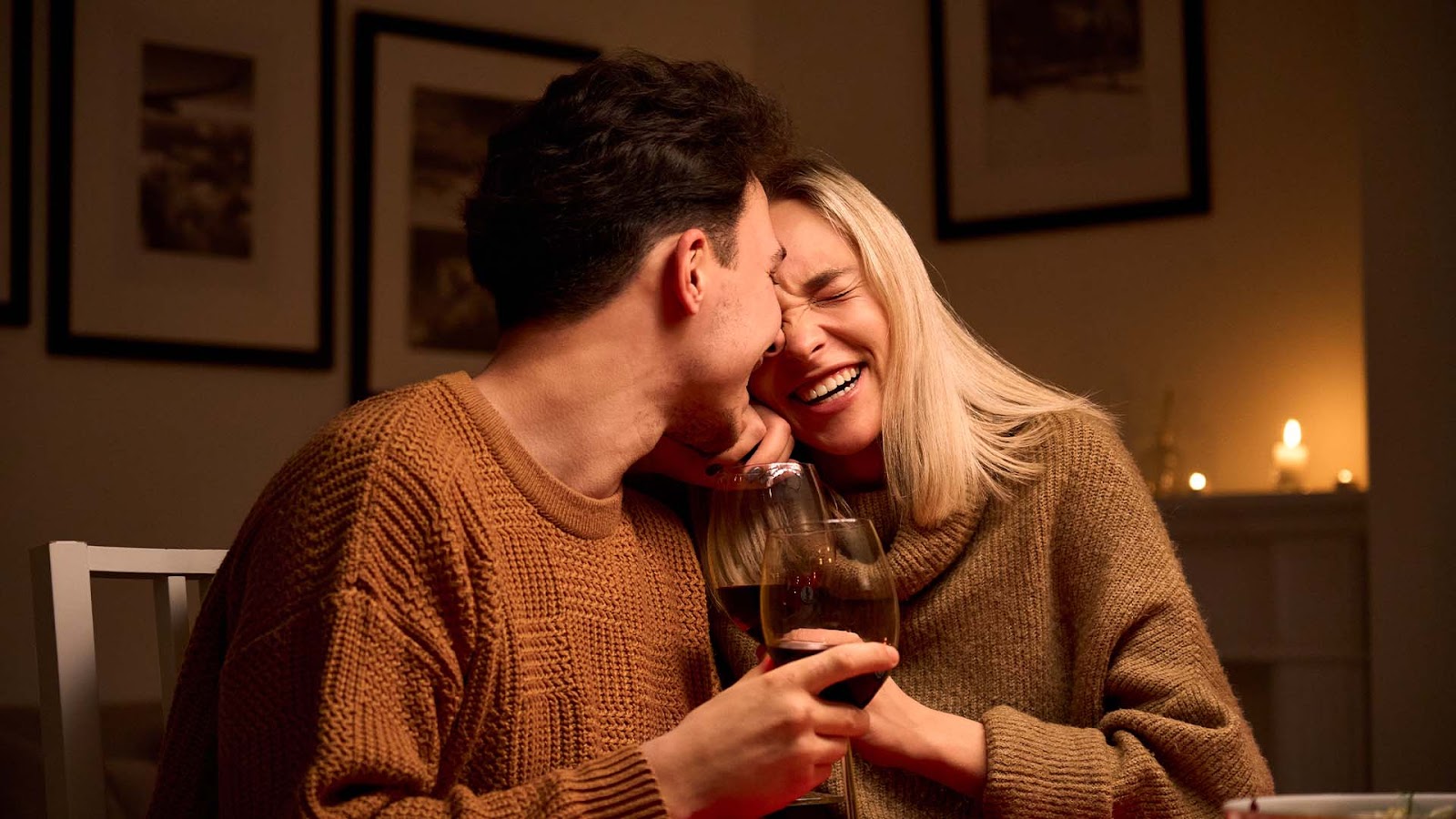 Brunette man and blonde woman in matching beige sweaters laughing while drinking wine