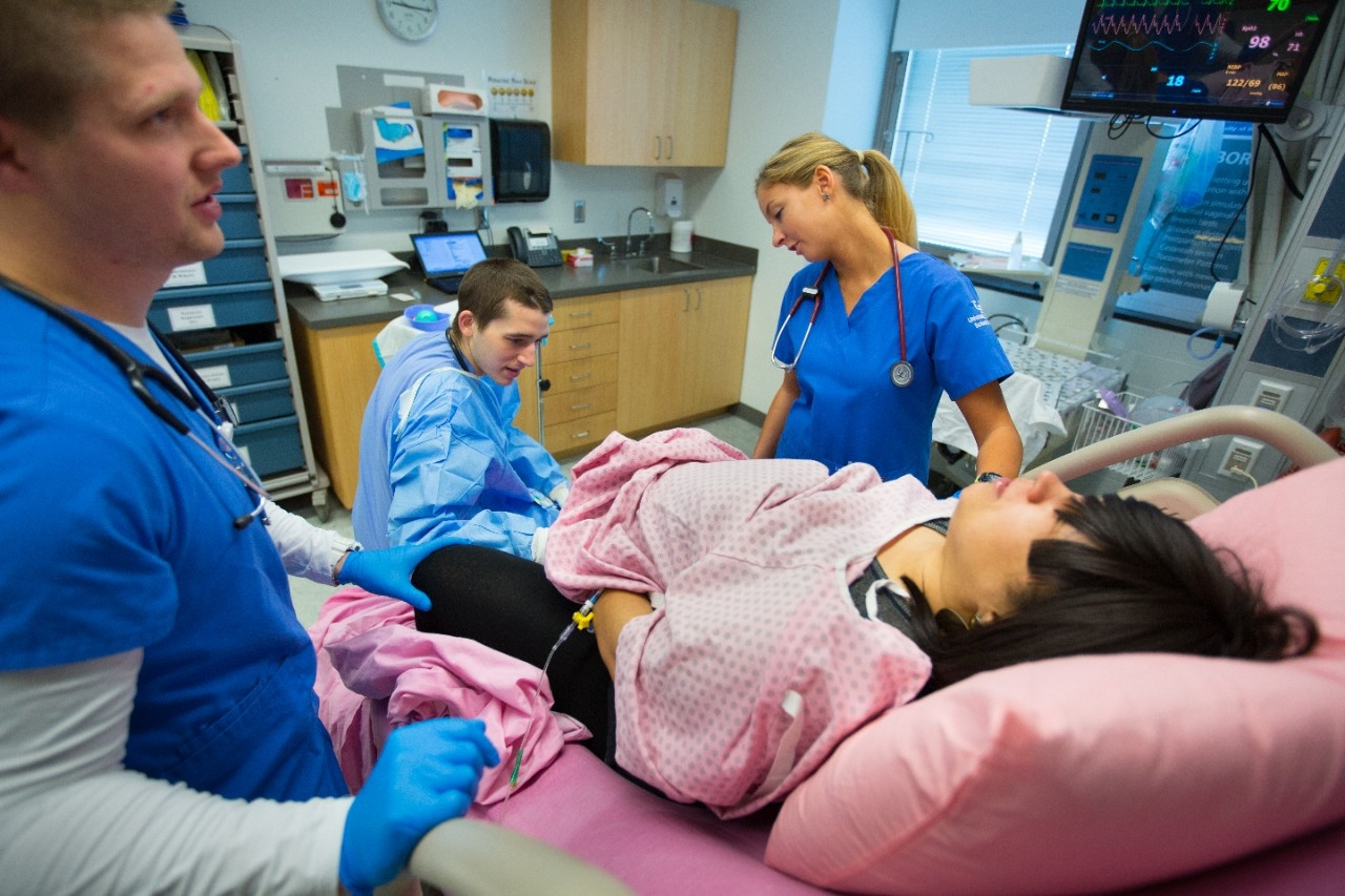 A group of medical students practicing clinical skills on mannequins in a training room with a faculty member observing and guiding their progress.