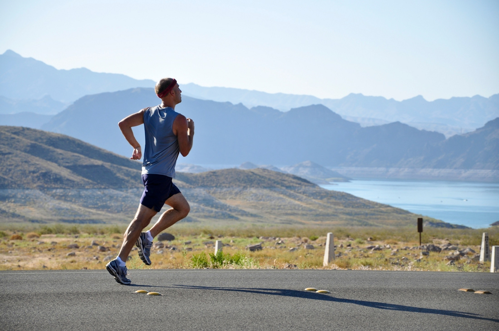 Man Running on Roadside With A Mountains and a Lake in the Background.