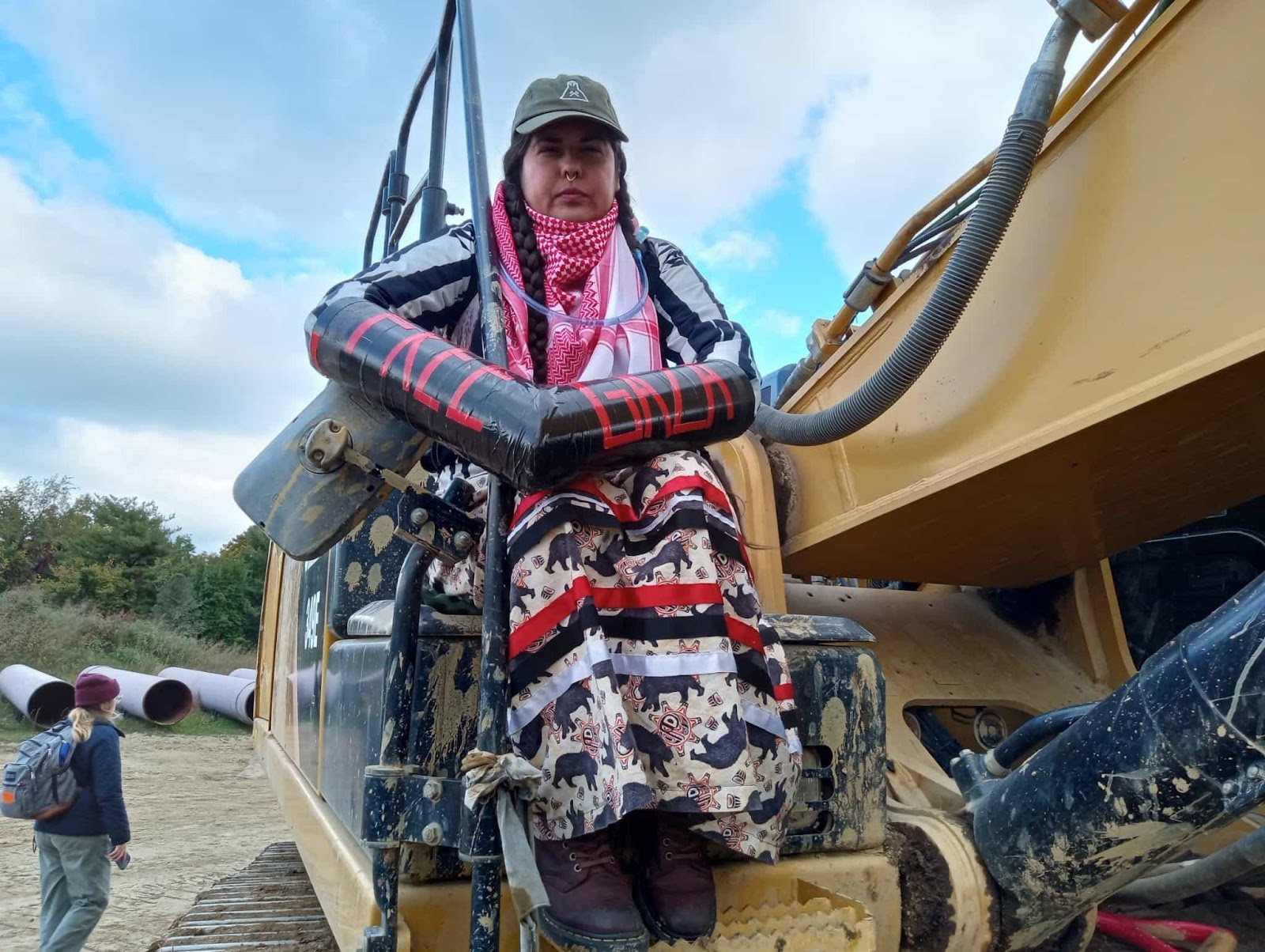 An indigenous American protester sits on a construction vehicle, her arm lock saying Free Gaza