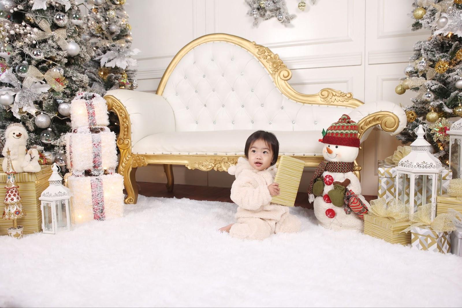 newborn christmas photo idea: baby wearing a bear jumpsuit playing with a present in a white christmas setup