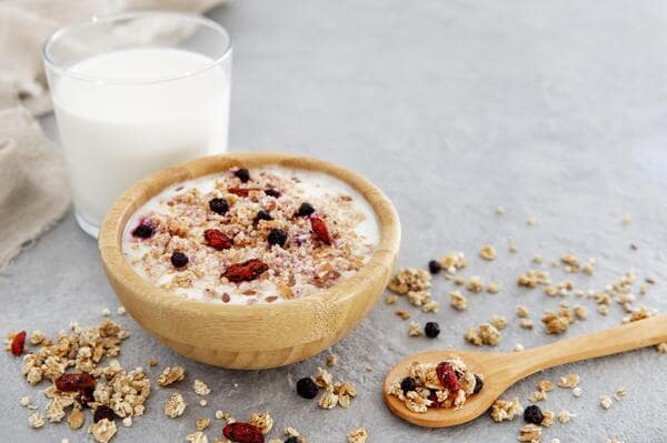 A wooden bowl filled with cereals and a glass of milk on the side