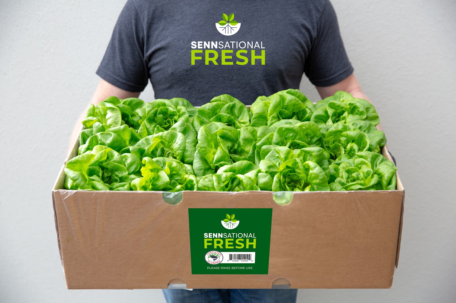 A person in a Sennsational Fresh tshirt holding a cardboard box of fresh lettuce greens