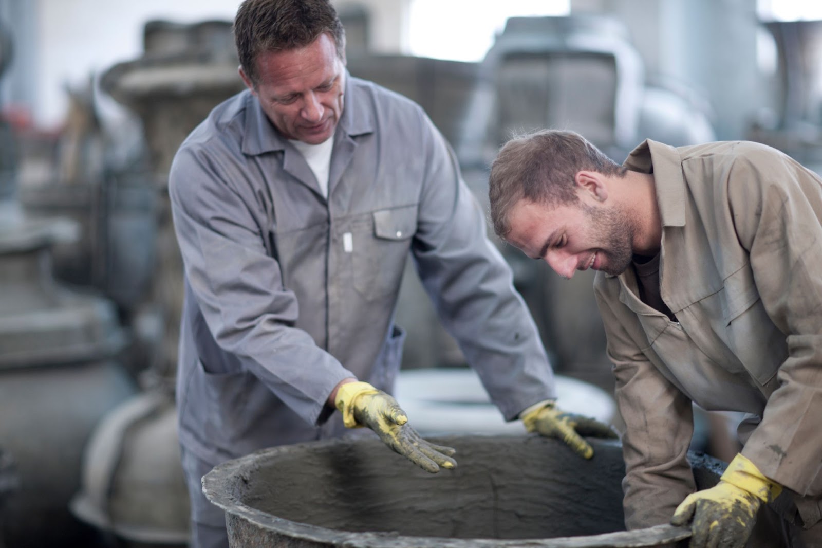 Two men working near a container of concrete. 