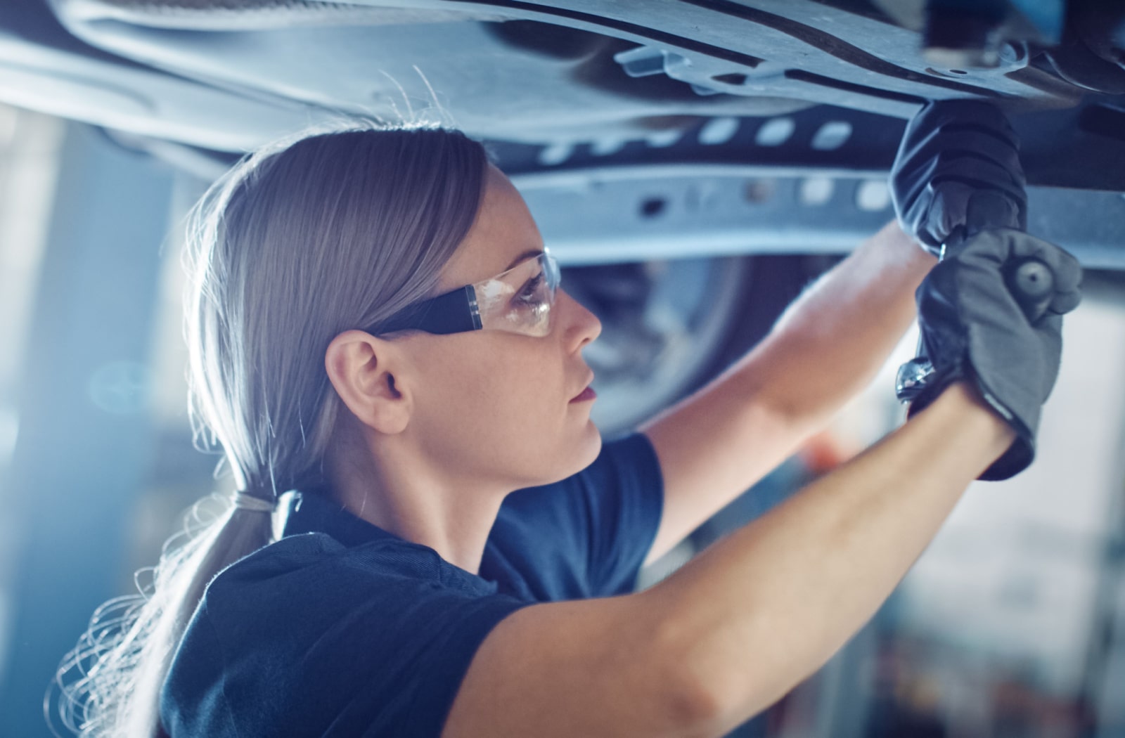 A female mechanic working on a car and wearing prescription safety glasses