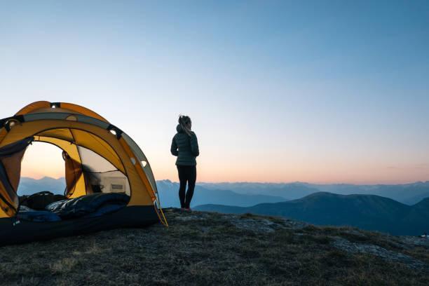 Young woman watches sunrise outside camping tent Sun rises over distant Swiss Alps outdoor adventures stock pictures, royalty-free photos & images