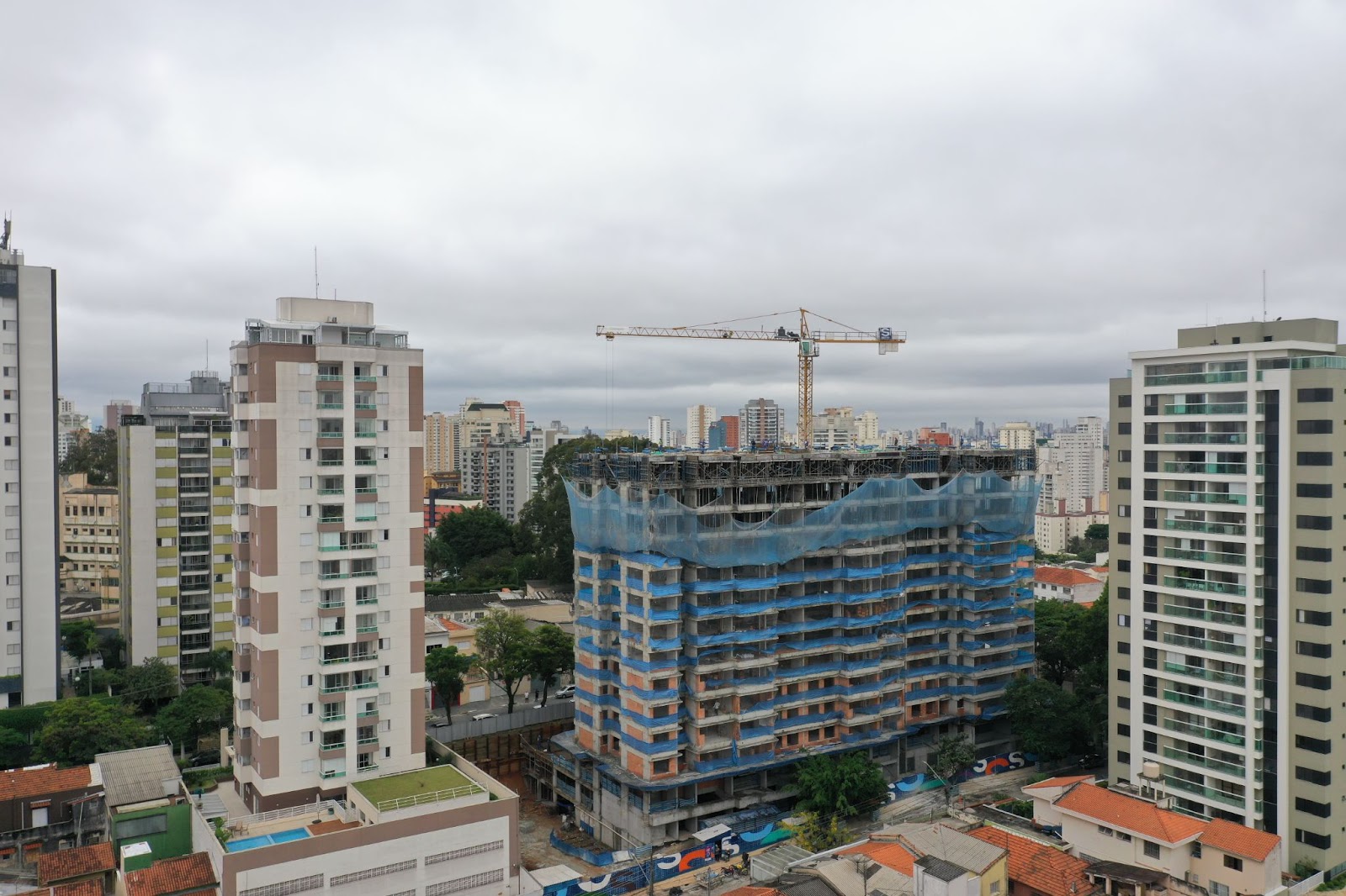 Foto que mostra apartamento em construção, com vários prédios em volta e com um céu meio cinza.