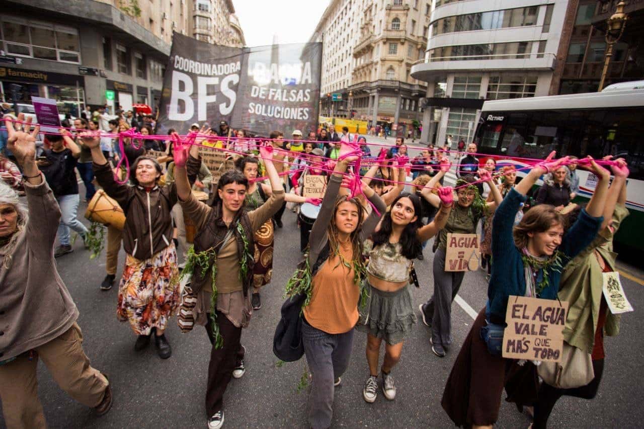 Dozens of rebels hold up their hands, all connected by pink ribbons, as they march through the Argentine capital