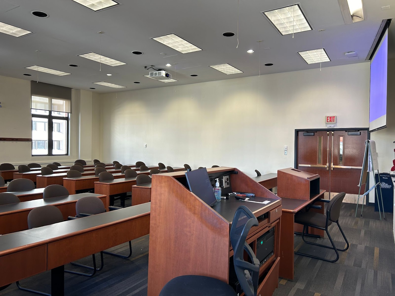 View from the front of the room: Lectern, computer monitor, projector and screen.