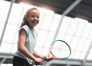 ילדה צעירה מחייכת ואוחזת מחבט טניס