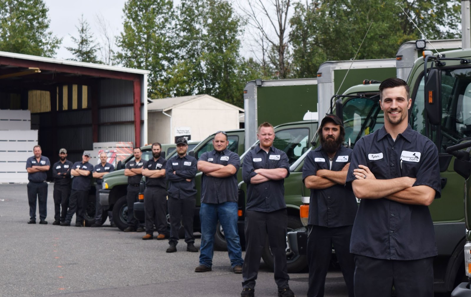 A descending row of Equipment Experts semi truck repair technicians smiling with arms folded